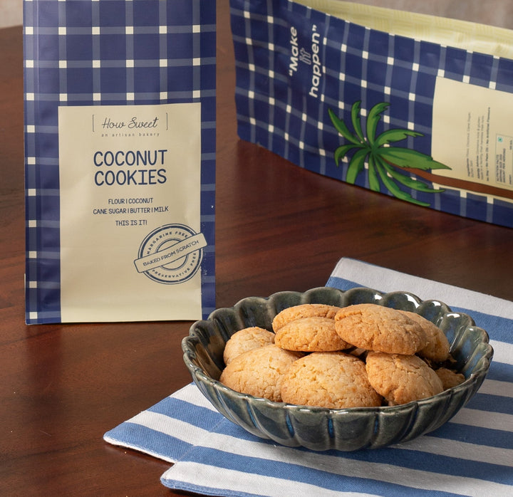 Coconut cookies in a blue and white checkered package on a wooden table with a bowl of cookies and a cup.