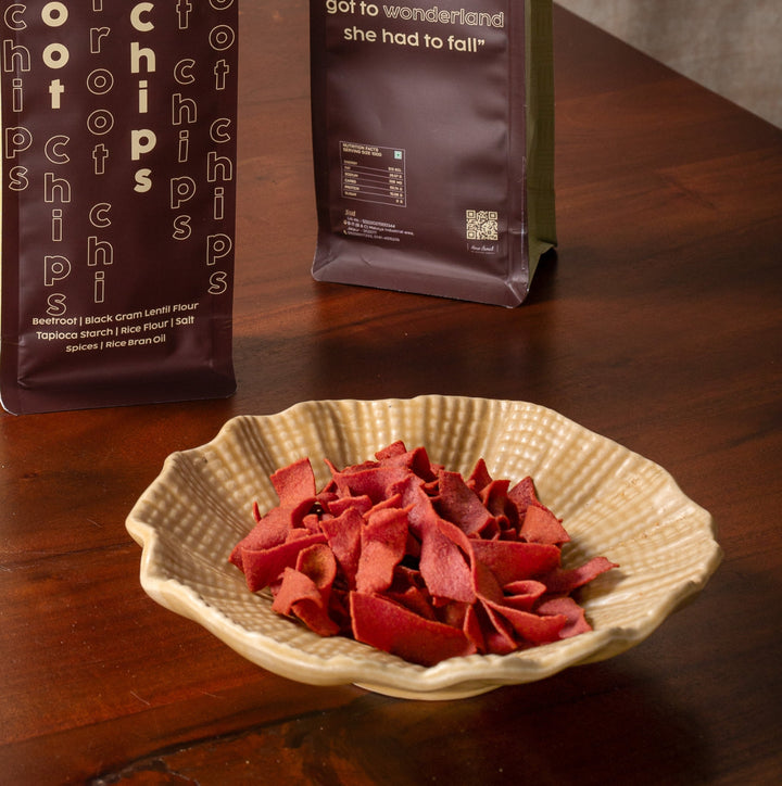 Two packages of beetroot chips on a wooden table with a bowl of chips in front.